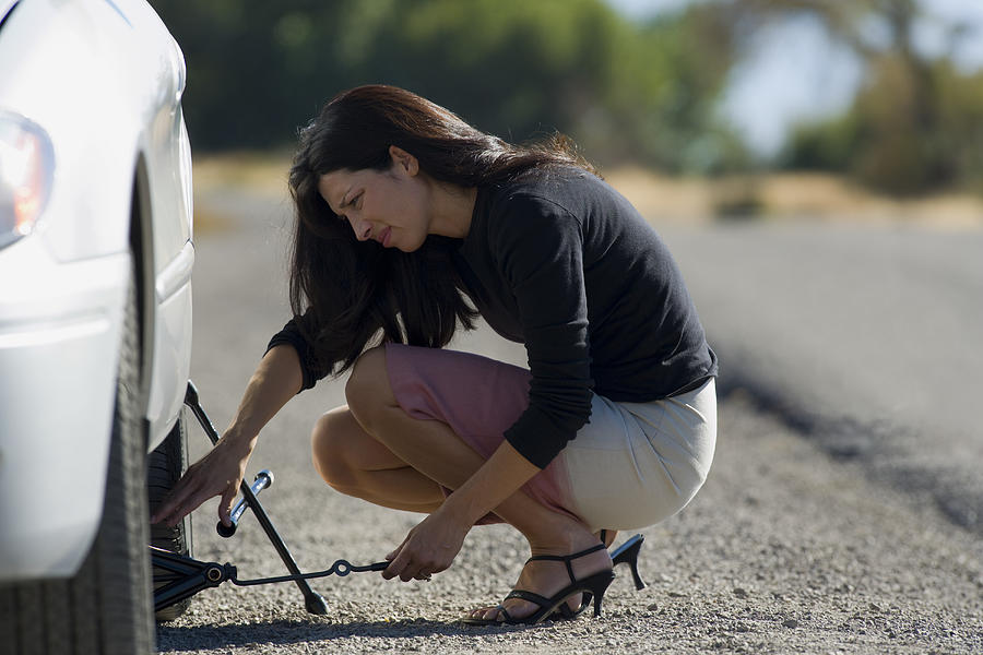 Profile of a woman fixing a flat tire Photograph by Rubberball
