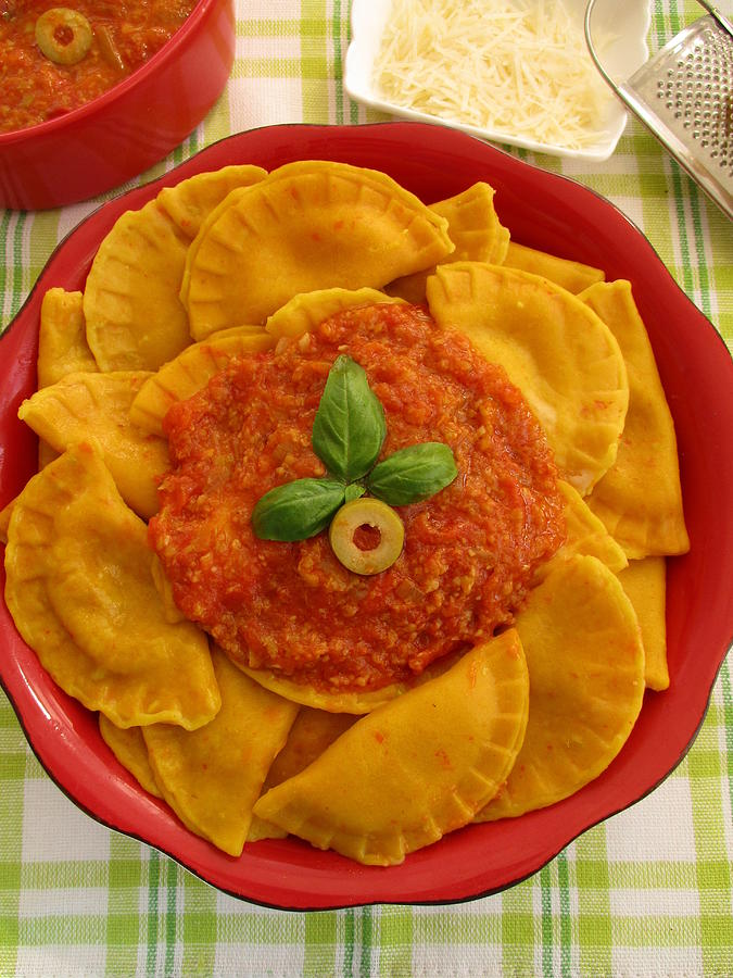 Pumpkin ravioli with tomato and olive sauce in red bowl Photograph by Tanai