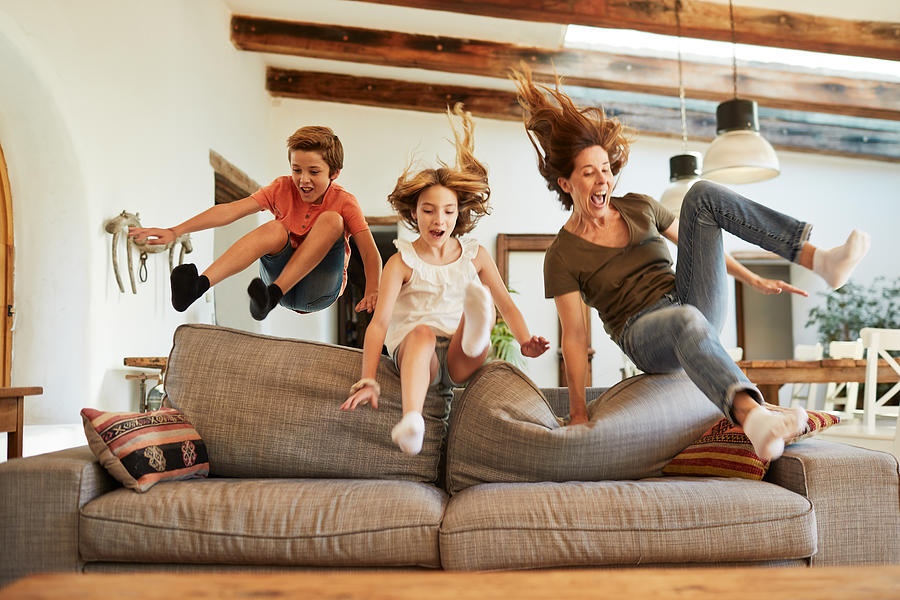 Race for the best spot on the sofa. Mother and children jumping. Photograph by Tempura