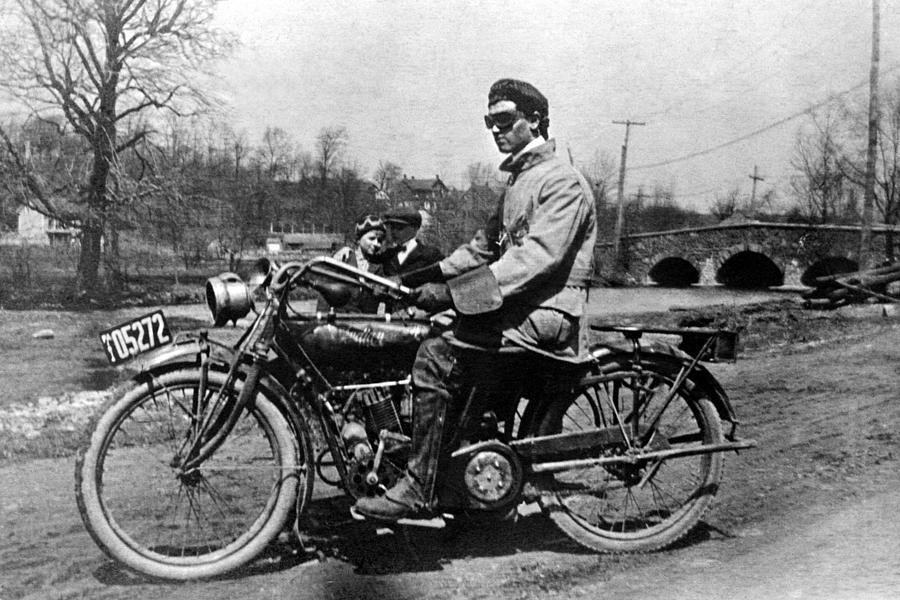 Rakish motorcyclist sitting on bike,1909 Man and woman standing in background Photograph by Thinkstock Images
