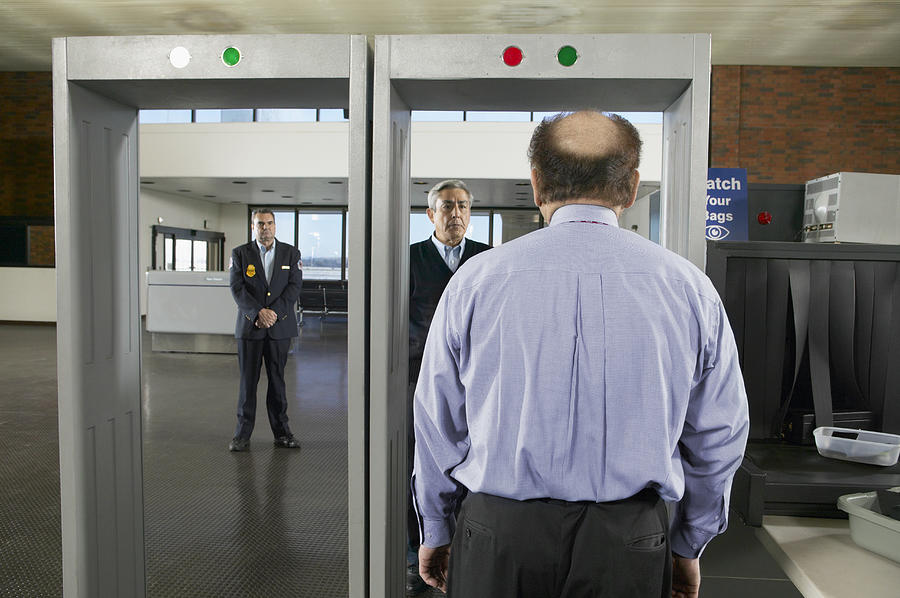 Rear View of a Balding Man Walking Through an Airport Metal Detector Photograph by Digital Vision.