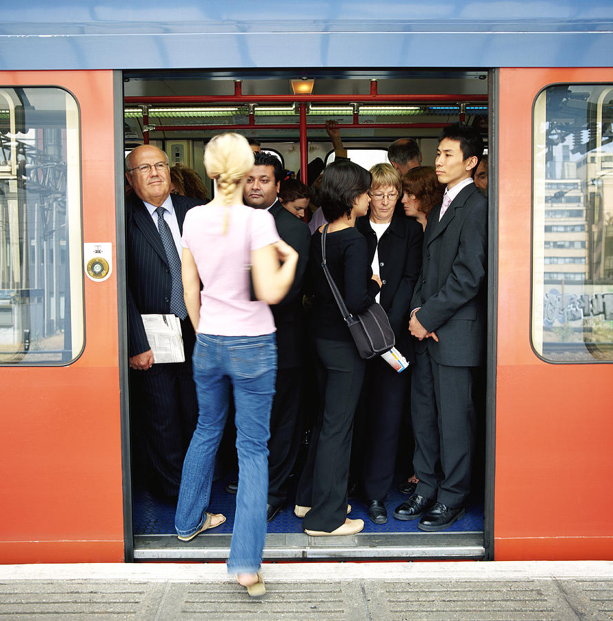 Rear View of a Blonde Woman Stepping Onto a Crowded Commuter Train Photograph by Digital Vision.