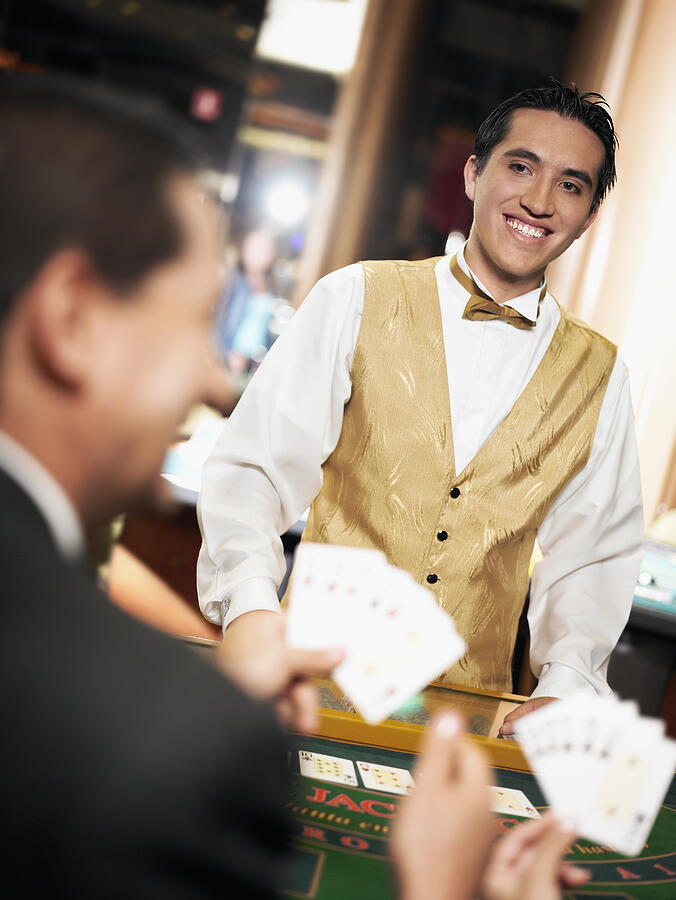 Rear view of a mature man holding playing cards with a casino worker standing in front of him Photograph by Glowimages