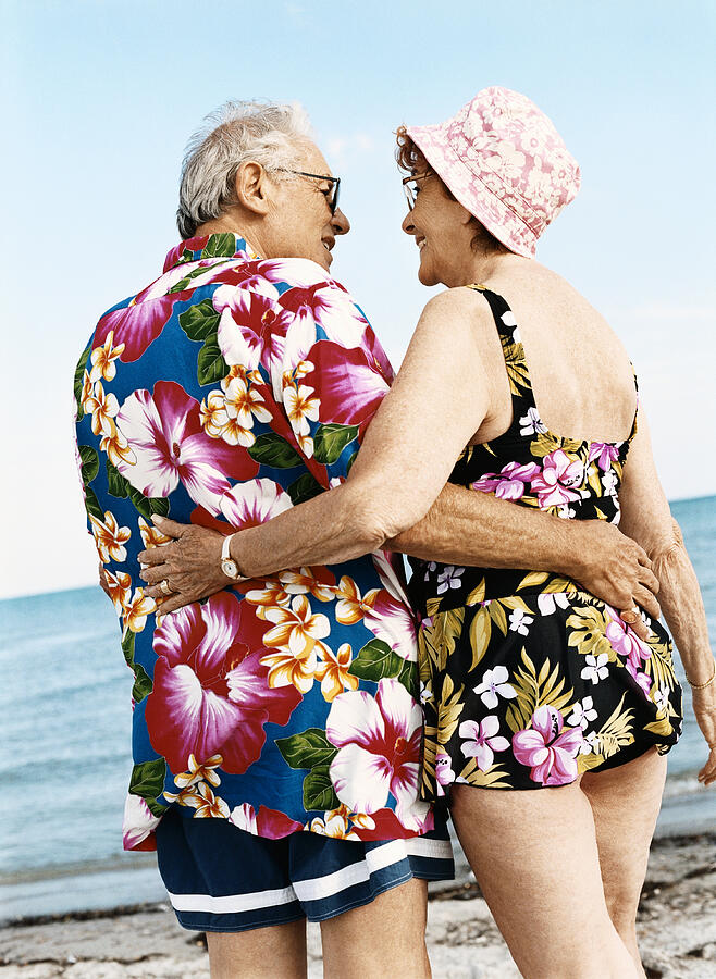 Rear View of a Senior Couple in Colourful Swimwear Standing on the Beach With Their Arms Around Each Other Photograph by Digital Vision.