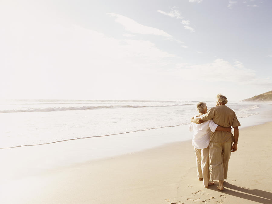 Rear View of a Senior Couple Walking on a Beach With Their Arms Around Each Other Photograph by Digital Vision.