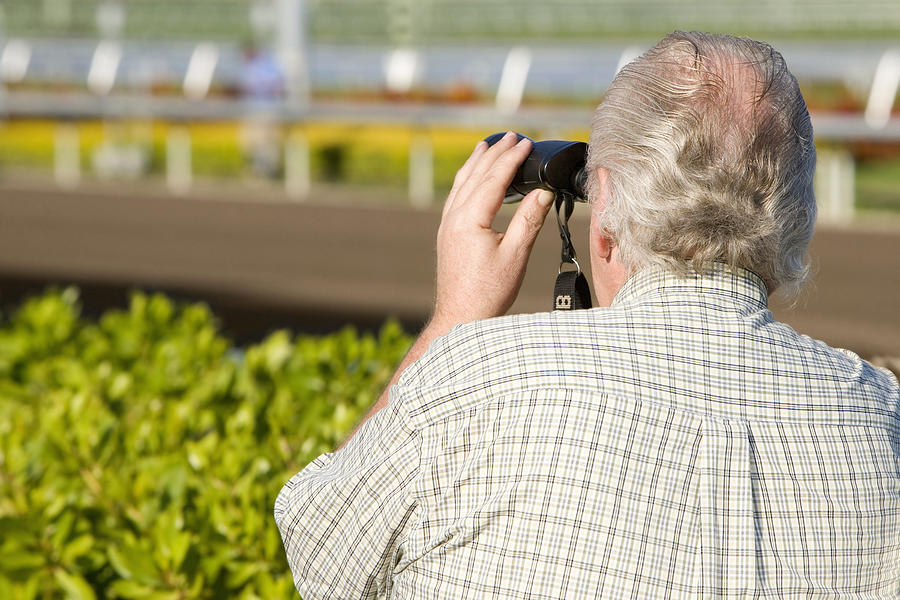 Rear view of a spectator looking through a pair of binoculars at the horseracing track Photograph by Glowimages