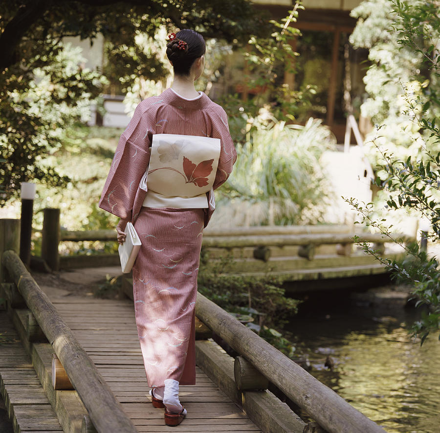 Rear View of a Woman Holding a Book and Walking on a Wooden Bridge Photograph by Digital Vision.