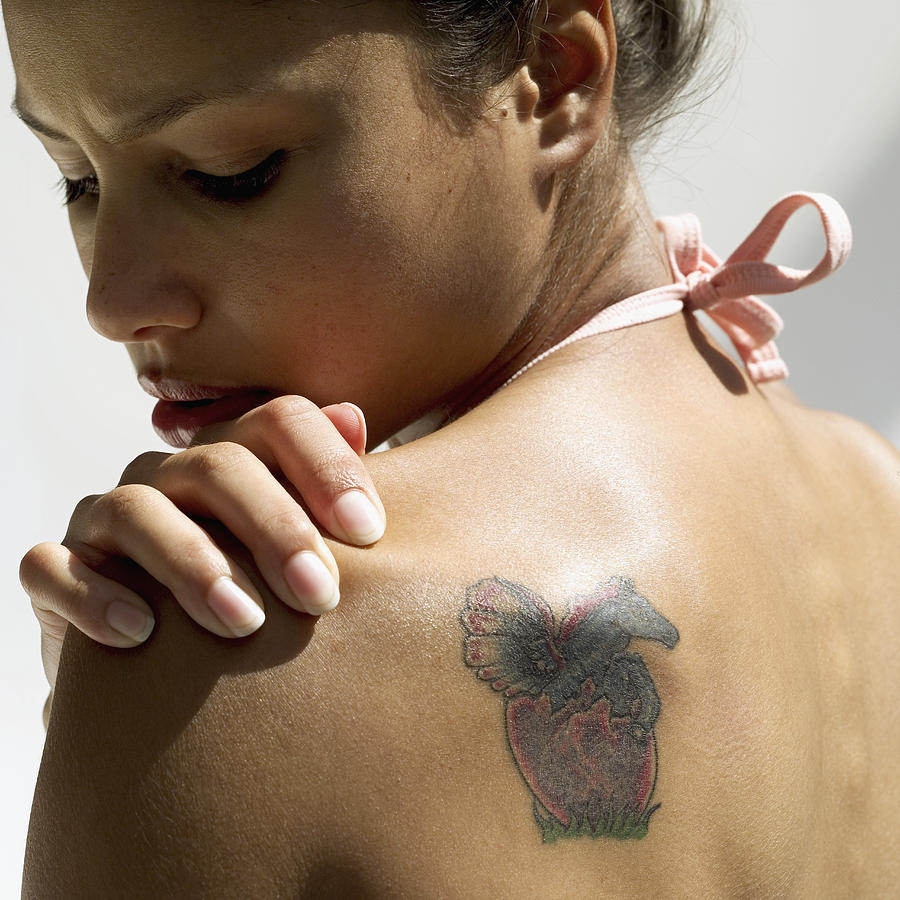 Rear view of a young woman looking at a tattoo on her back Photograph by Stockbyte