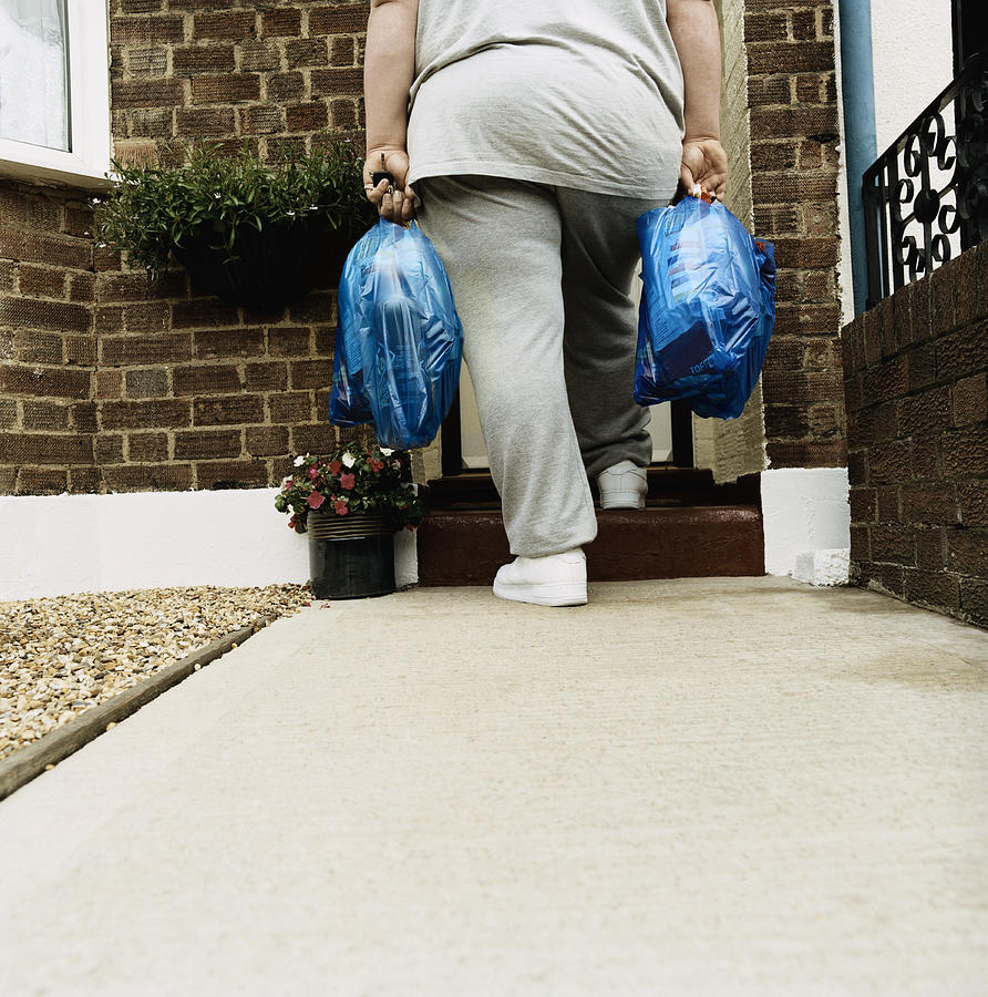 Rear View of an Overweight Person Standing With Shopping Bags on a Doorstep Photograph by Digital Vision.