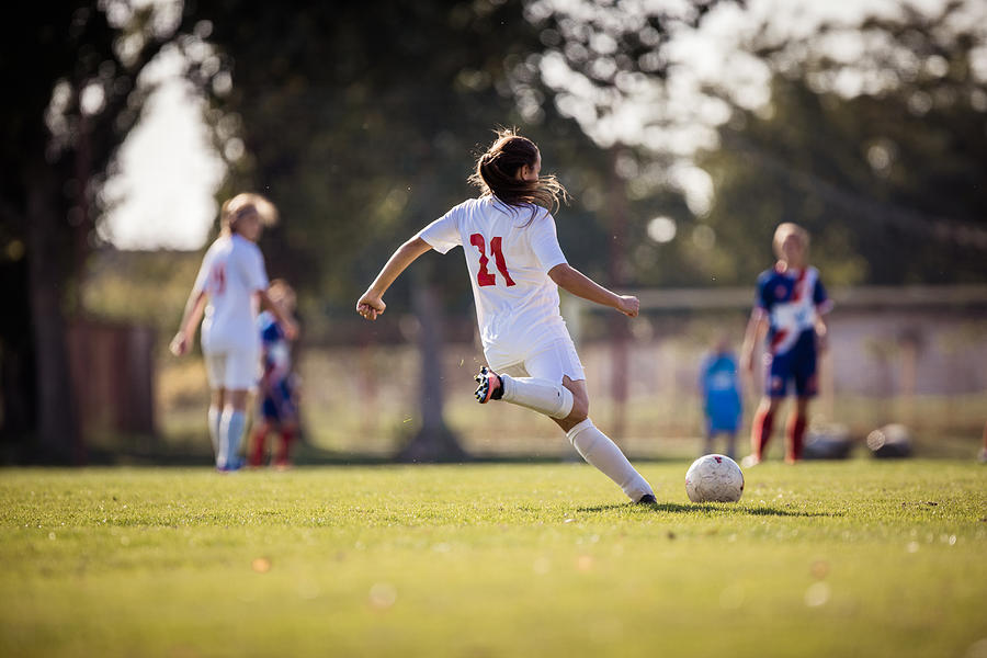 Rear view of determined female soccer player kicking the ball on a match. Photograph by Skynesher