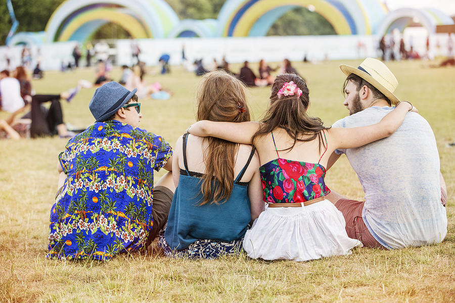 Rear view of friends sitting on grass at festival Photograph by Igor Emmerich