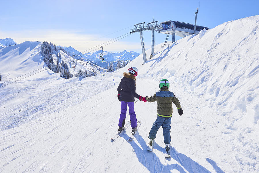 Rear view of girl and brother holding hands on ski slope, Gstaad, Switzerland Photograph by Jakob Helbig