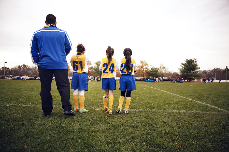Rear view of soccer players standing with coach on playing field Photograph by Cavan Images