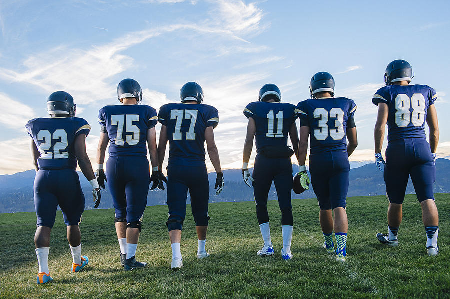Rear view of teenage and young adult american football team in a row Photograph by Pete Saloutos