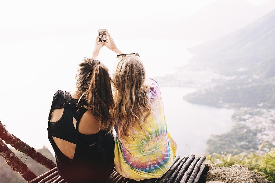 Rear view of two female friends taking smartphone selfie at Lake Atitlan, Guatemala Photograph by Kate Ballis
