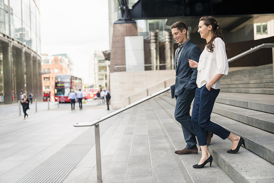 Rear view of young businessman and woman chatting whilst walking down stairway, London, UK Photograph by Ben Pipe Photography