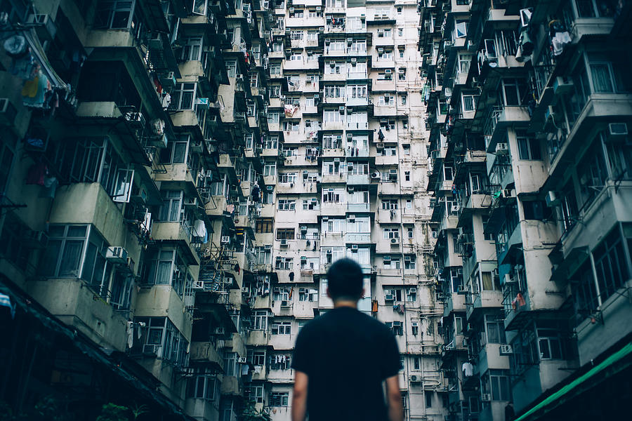 Rear view of young man surrounded by old traditional residential buildings and lost in city Photograph by D3sign