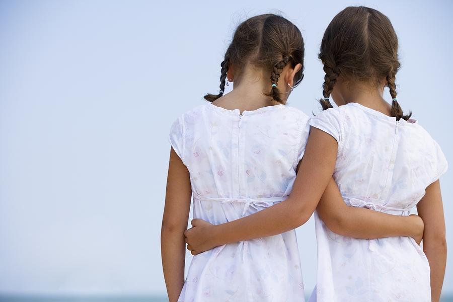 Rear view of young sisters wearing matching dresses and hugging outdoors Photograph by Terry Vine