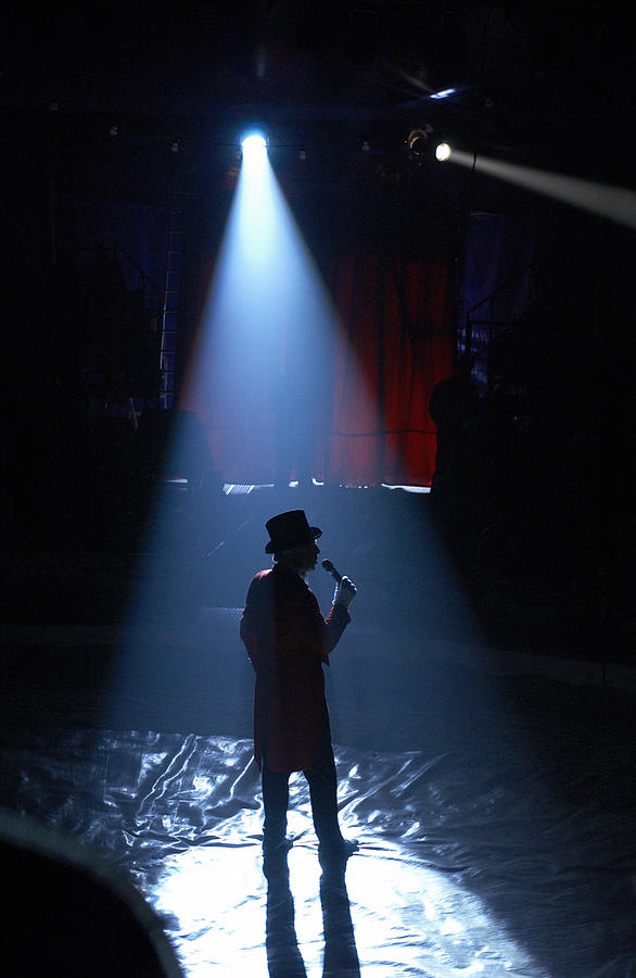 Rear View Silhouette of a Spot lit Ringmaster Standing in a Circus Ring, Talking into a Microphone Photograph by Adrian Peacock
