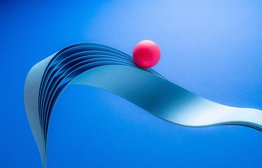 Red ball riding paper wave Photograph by PM Images