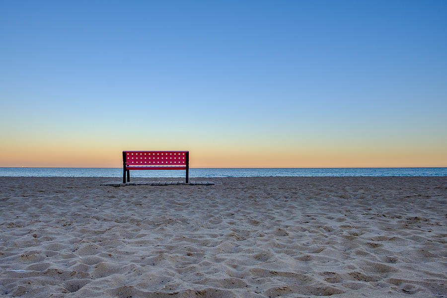 Red empty bench at the beach at sunset, sand in foreground and ocean in backround Photograph by Finn Bjurvoll Hansen