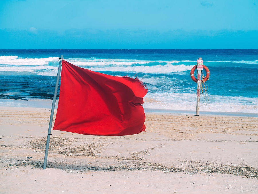 Red flag and lifebelt attached to post on the beach Photograph by Photo by Rafa Elias