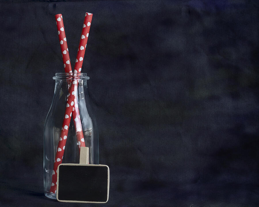 Red paper straws with shapes heart in empty glass bottle against abstract background. Subject captured againt soft window lighting an copy space Photograph by Rosa María Fernández Rz