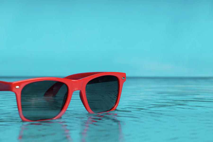 Red sunglasses in blue water, the concept of relaxing on the beach