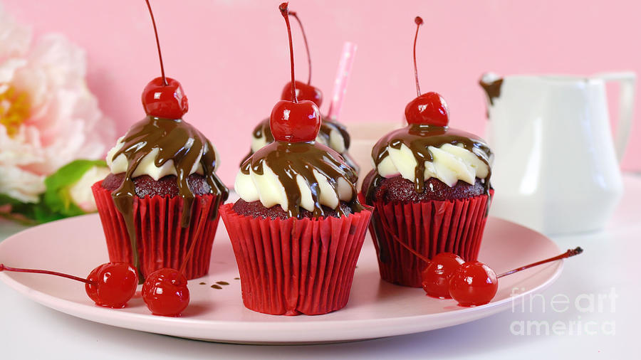 Red velvet cupcakes with chocolate sauce and cherries. Photograph by Milleflore Images