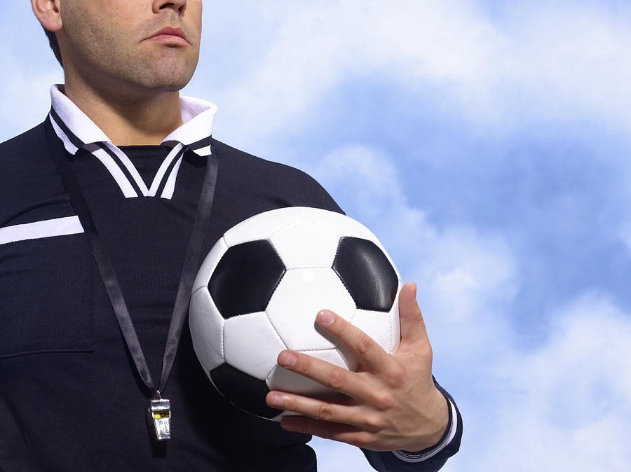 Referee holding football, with whistle around neck, mid section Photograph by Peter Dazeley