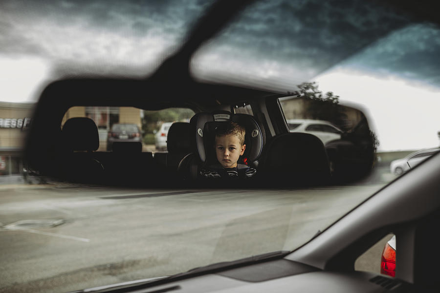 Reflection of boy on rear-view mirror in car Photograph by Cavan Images