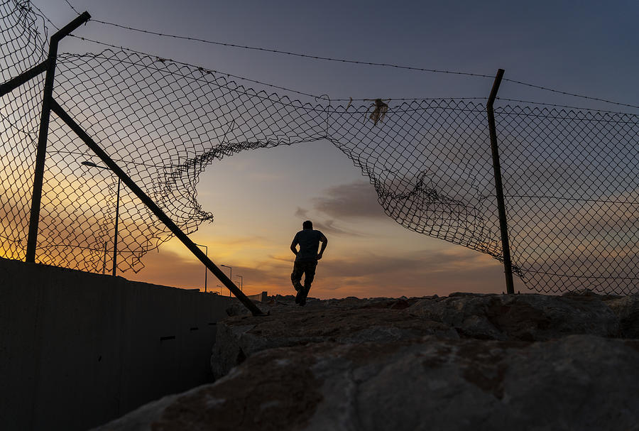 Refugee man running behind fence, Photograph by Ozgurdonmaz