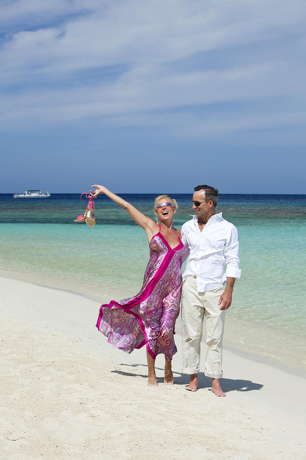 Relaxed adult couple walking along tropical beach Photograph by Dstephens