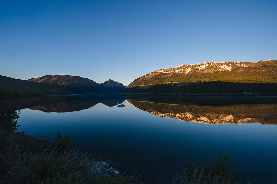 Remote mountains and blue sky reflected in still lake Photograph by Pete Saloutos