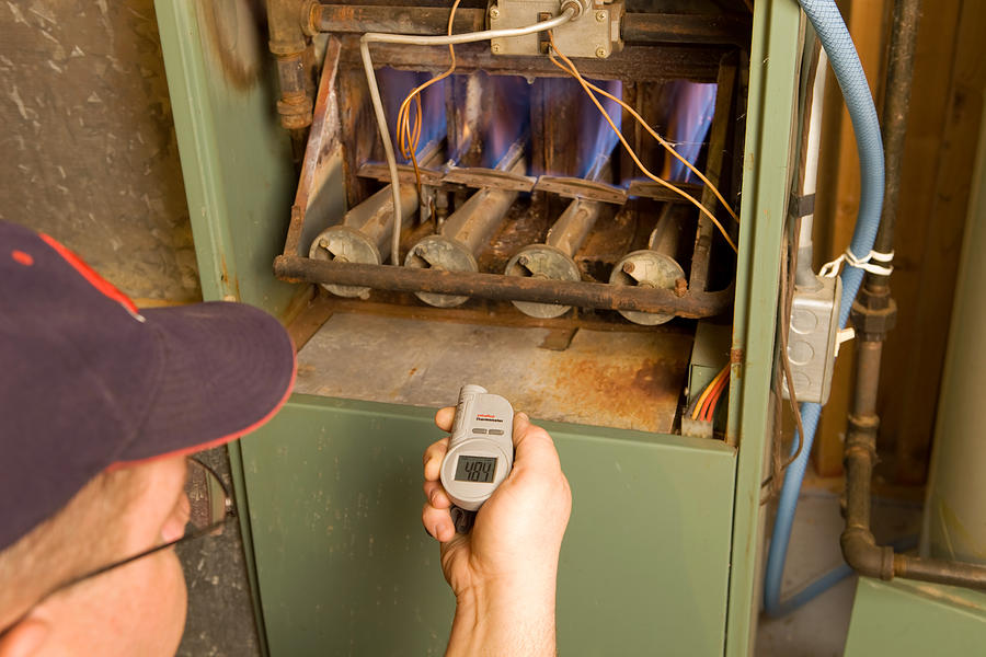 Repairman with Digital Infrared Thermometer Checks Gas Furnace Output Temperature Photograph by BanksPhotos