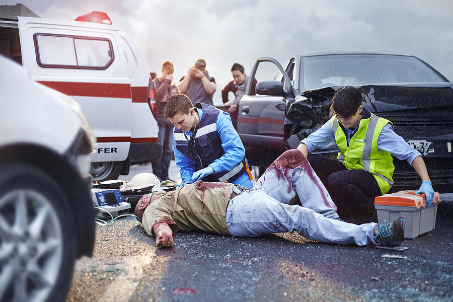 Rescue workers tending to bloody car accident victim in road Photograph by Caiaimage/Trevor Adeline