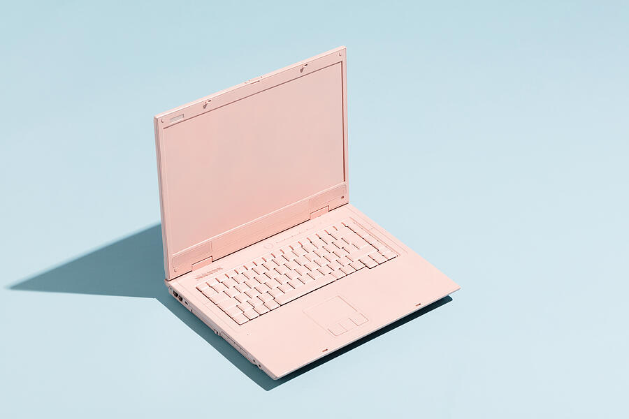 Retro pink laptop on a pastel blue background. Photograph by NiseriN