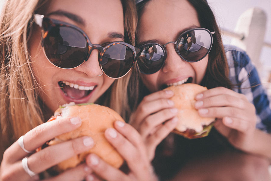 Retro style shot of teenage girl best friends eating burgers Photograph by Wundervisuals