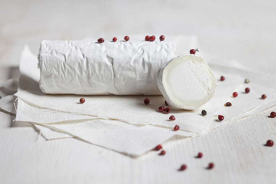 Roll of goats cheese camembert with red peppercorns on white cloth Photograph by Westend61
