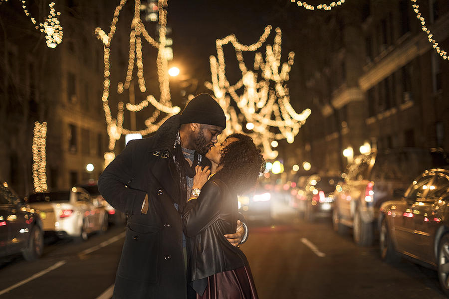 Romantic couple kissing by Christmas lights at night, New York, USA Photograph by Steve Prezant