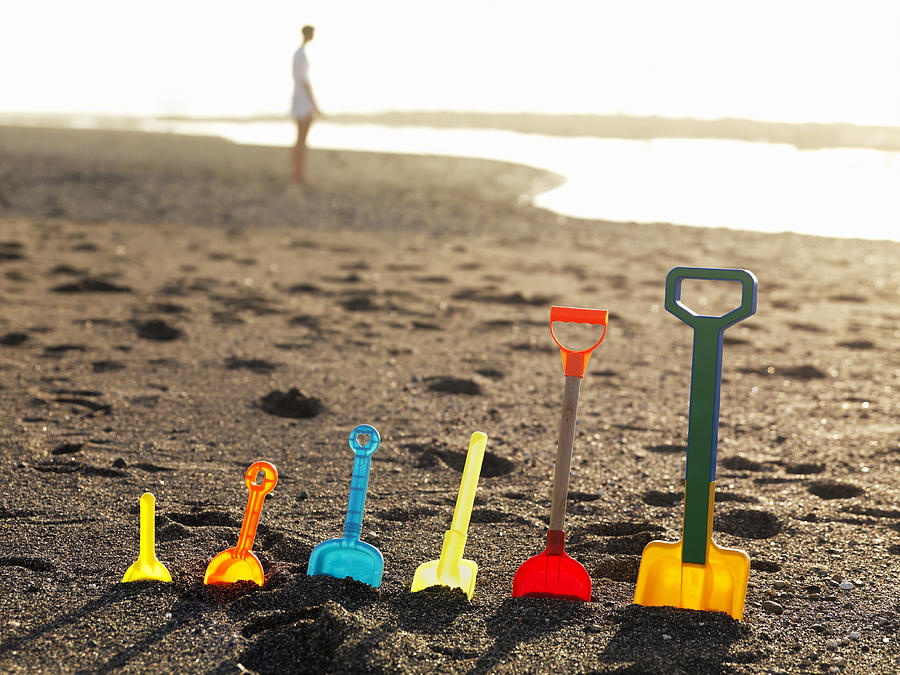 Row of assorted plastic spades standing in sand Photograph by Henrik Sorensen