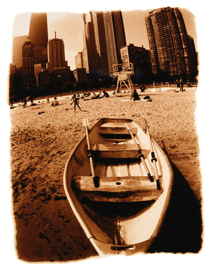 Rowboat stranded on beach, city behind Photograph by Stockbyte