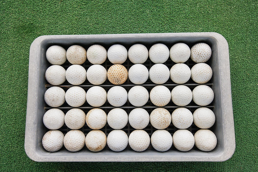 Rows of golf balls in tray on green Photograph by IPGGutenbergUKLtd
