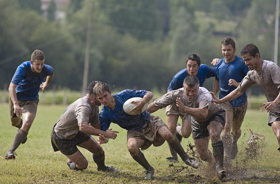 Rugby players covered with mud, tackling opponent Photograph by Photo and Co
