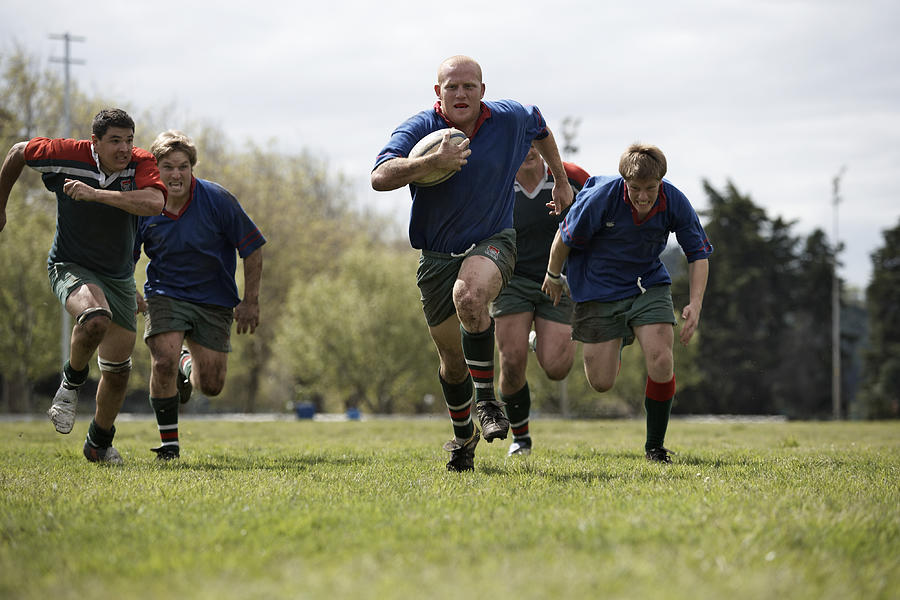 Rugby players running with ball on sports field Photograph by Alistair Berg