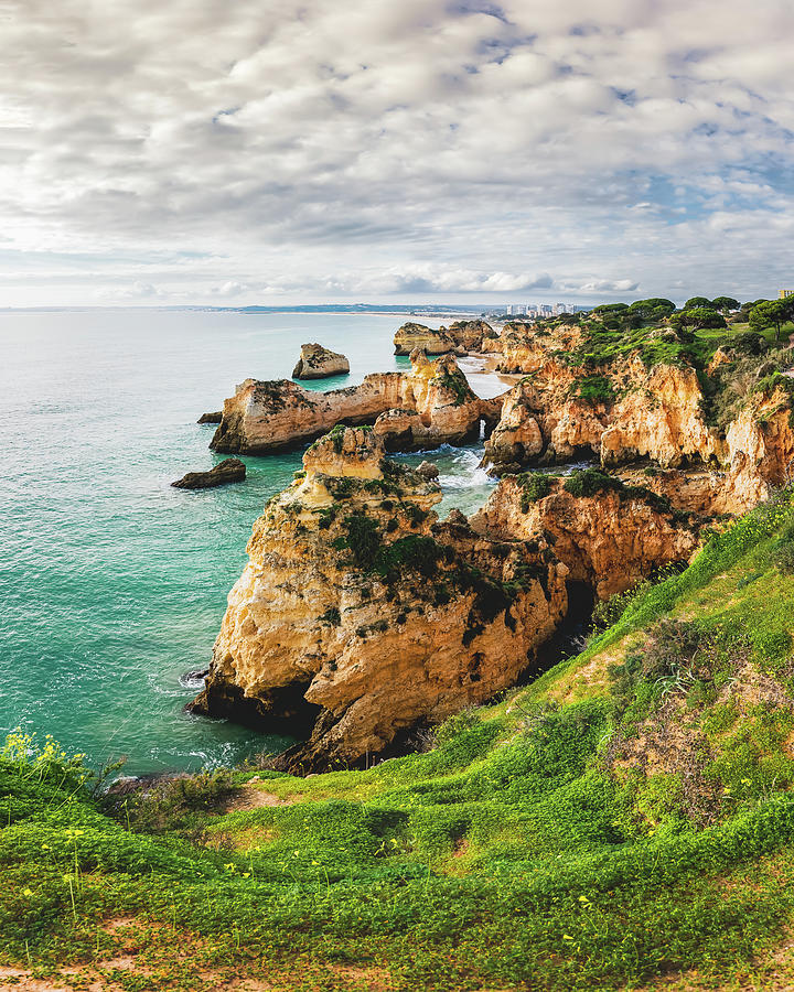 Rugged shoreline with cliffs and caves, set against the backdrop Photograph by Hanna Tor
