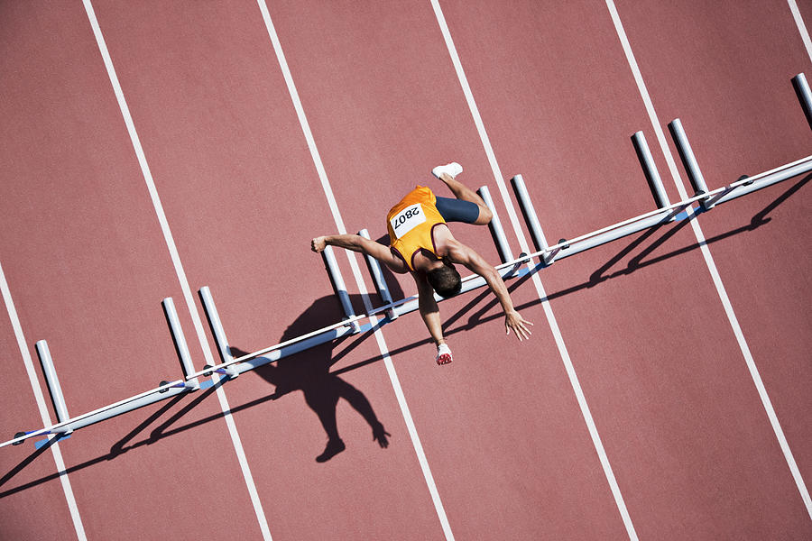 Runner jumping hurdles on track Photograph by Paul Bradbury