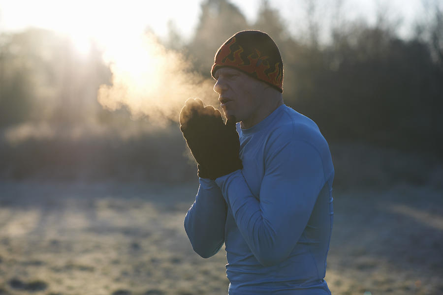 Runner wearing knit hat and gloves, rubbing hands together, breathing cold air Photograph by Peter Muller