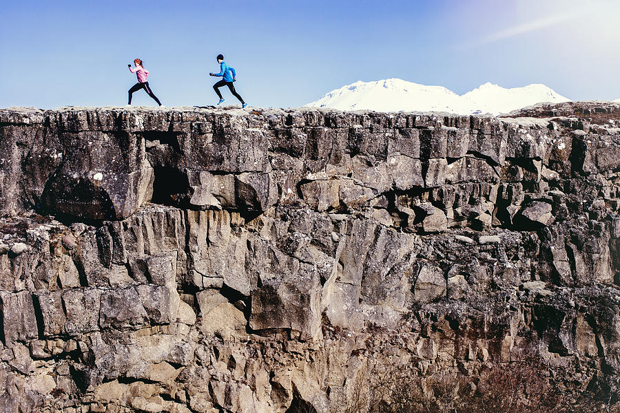 Running couple run along rock edge with mountains Photograph by Luca Sage