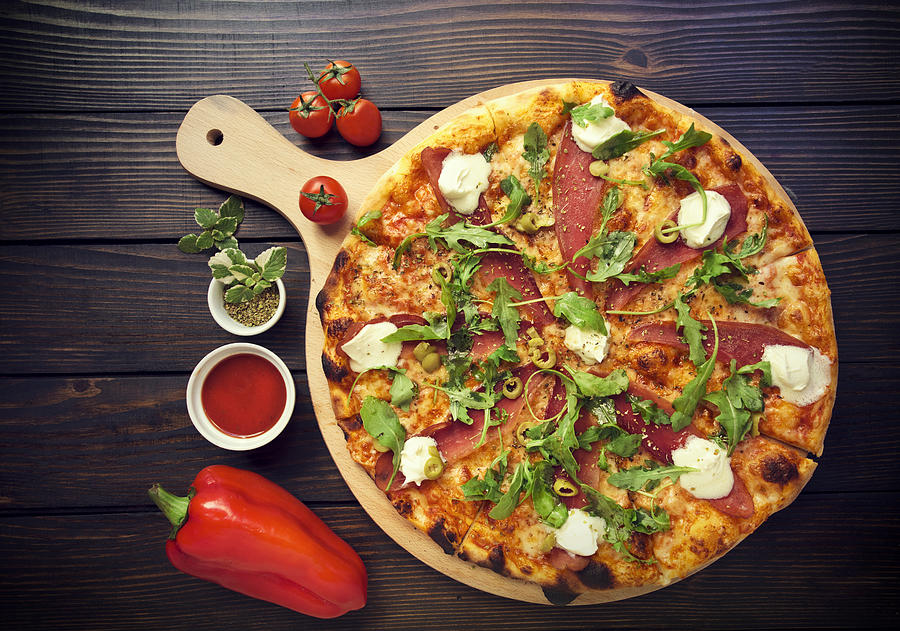 Rustic pizza with salami, olives and basil on wooden table Photograph by Zeljkosantrac